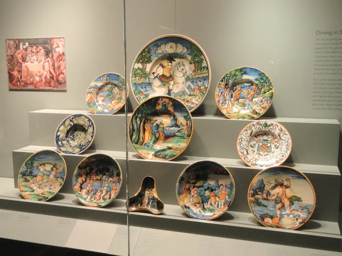 Ten colourful painted ceramic dishes arranged on tiered shelves inside a museum display case