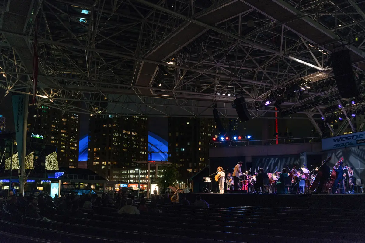 The WestJet Stage at night under a steel truss roof, with a performance under way.