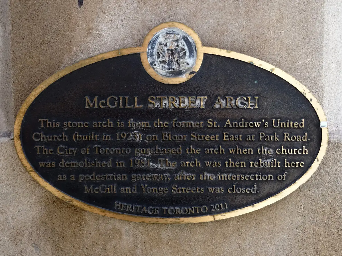 A dark oval plaque with gold lettering, reading McGill Street Arch, mounted on a stone wall
