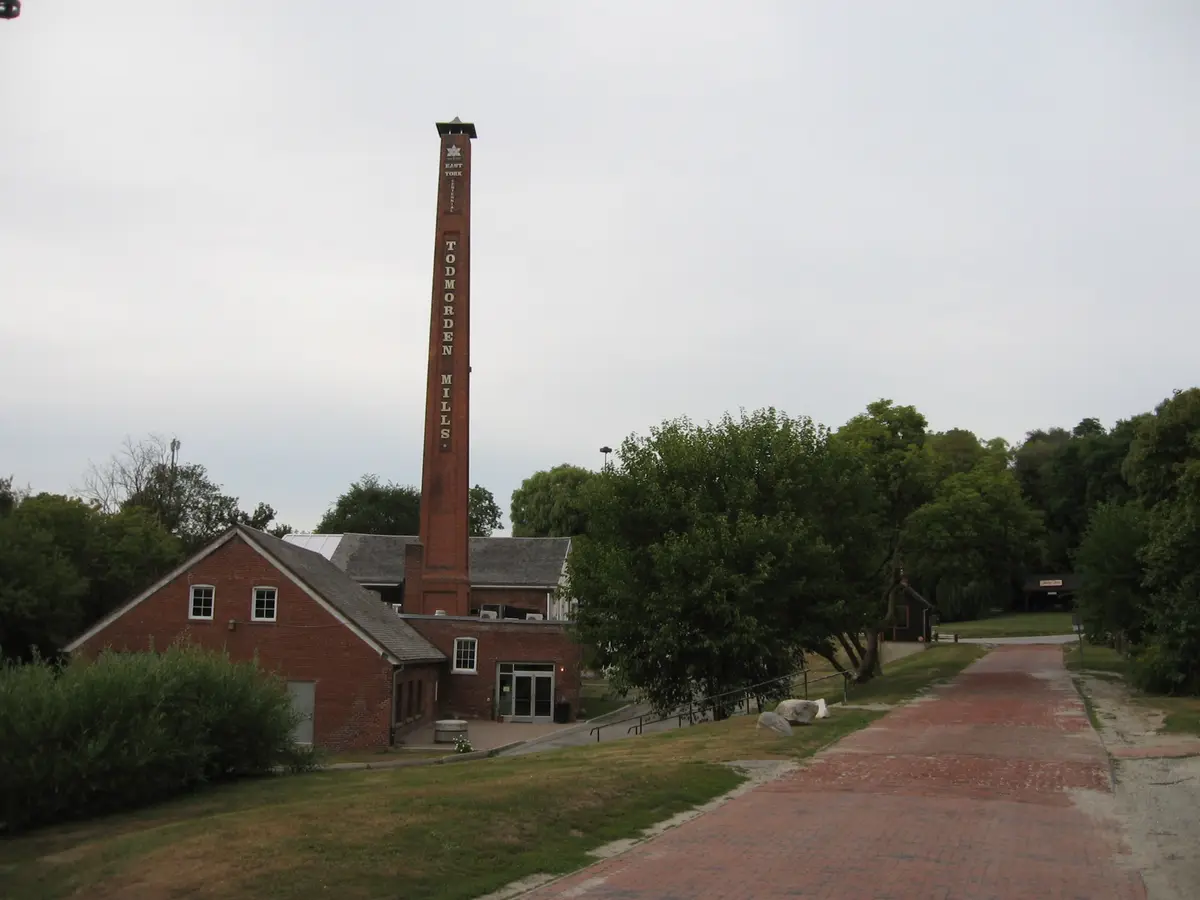 The restored Todmorden Mills paper mill and its tall brick chimney, seen from a brick path through the grounds.