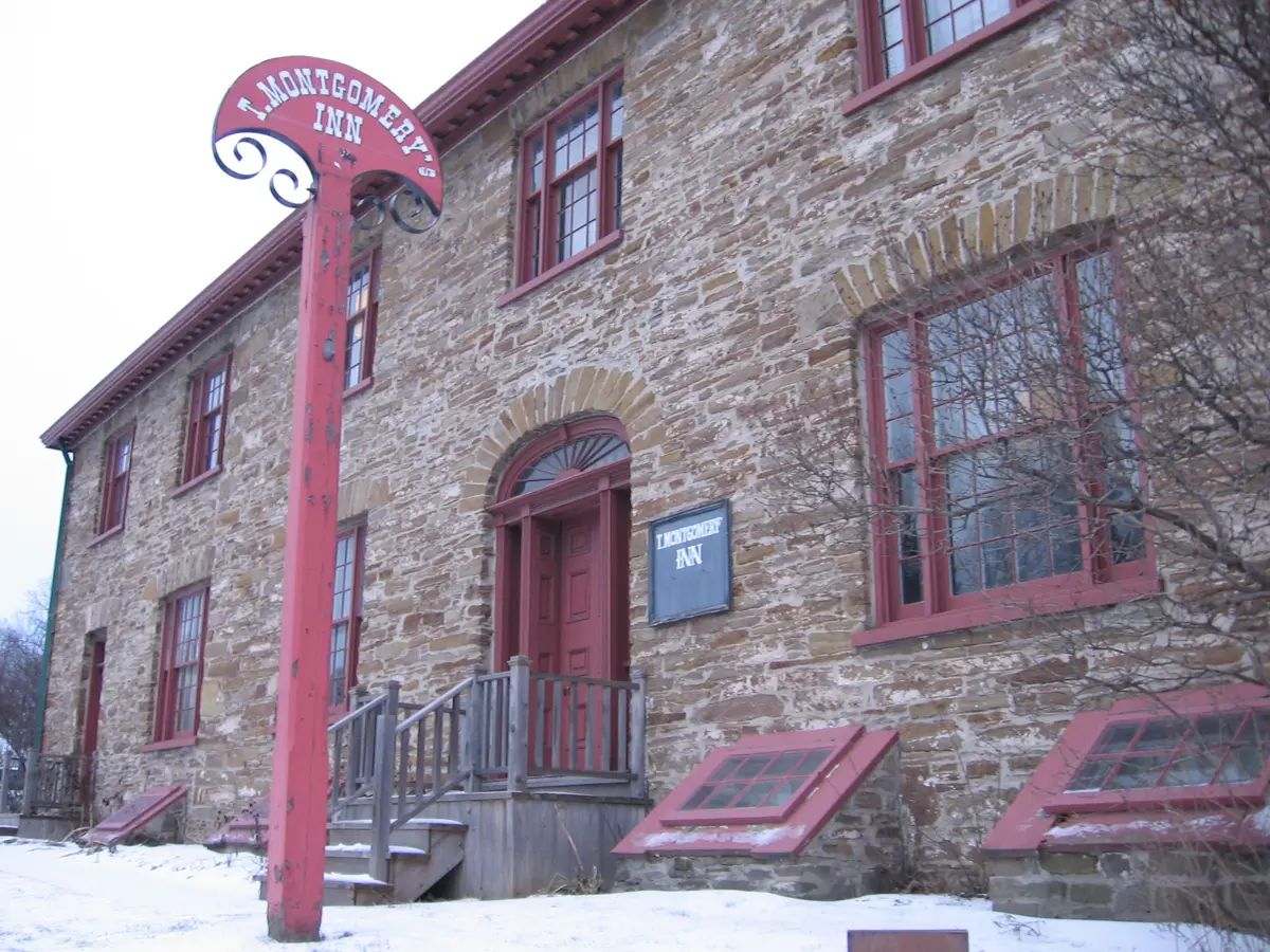 The red-trimmed fieldstone front of Montgomery's Inn under snow, with its painted sign post in the foreground