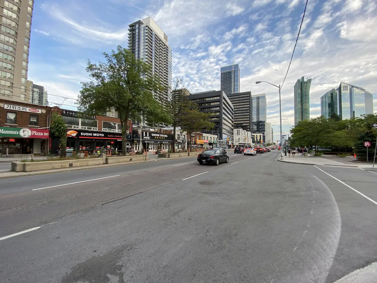 Yonge Street in Willowdale on a bright day, with shops along the left side and North York Centre towers rising in the distance