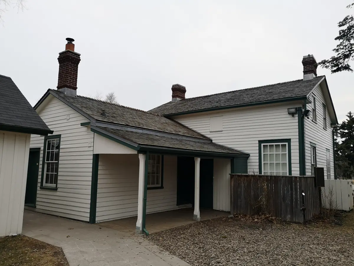 White clapboard Cornell House with a green-trimmed porch, a brick chimney and a gravel path in front