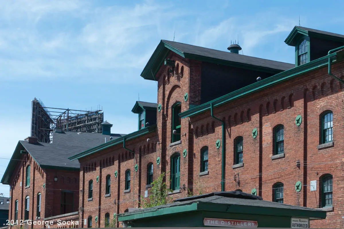 Red-brick distillery buildings with dark roofs and green trim, with round green plates on the brickwork