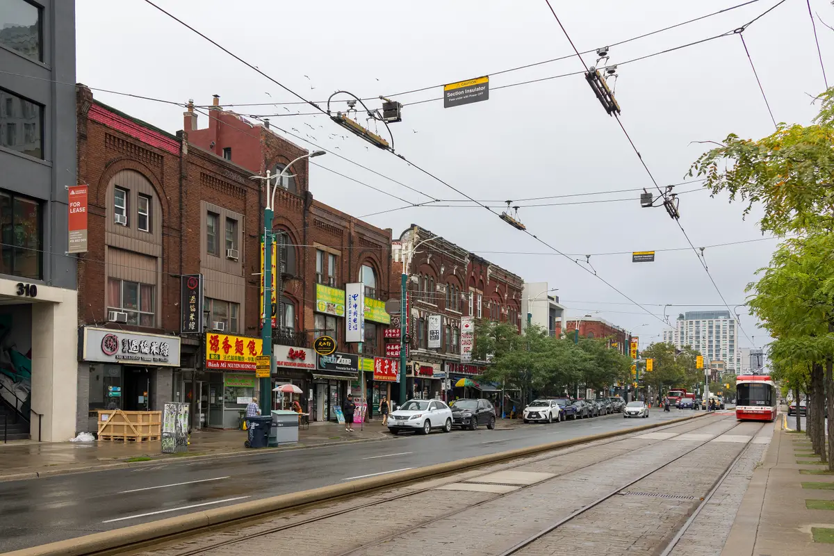 A streetcar on Spadina Avenue beside rows of brick storefronts with Chinese-language signs on the west side north of Dundas Street