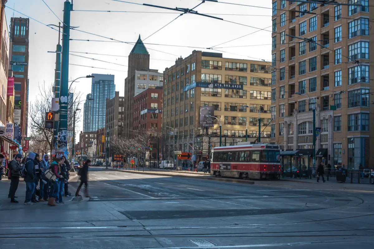 A red and white streetcar crossing a wide Spadina Avenue intersection, with brick and glass buildings on either side