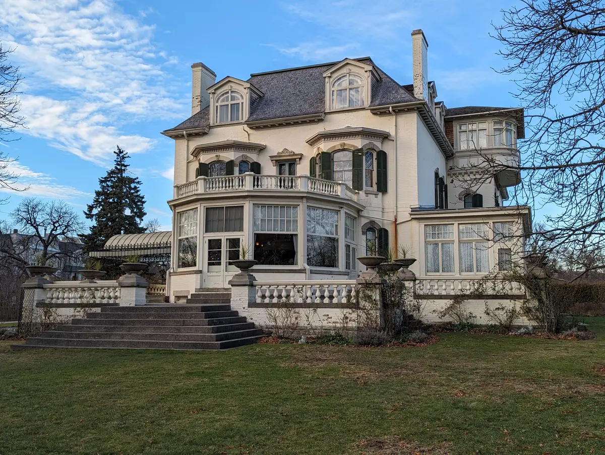 The pale, many-windowed back of Spadina House seen across a lawn and stone steps, under a blue winter sky