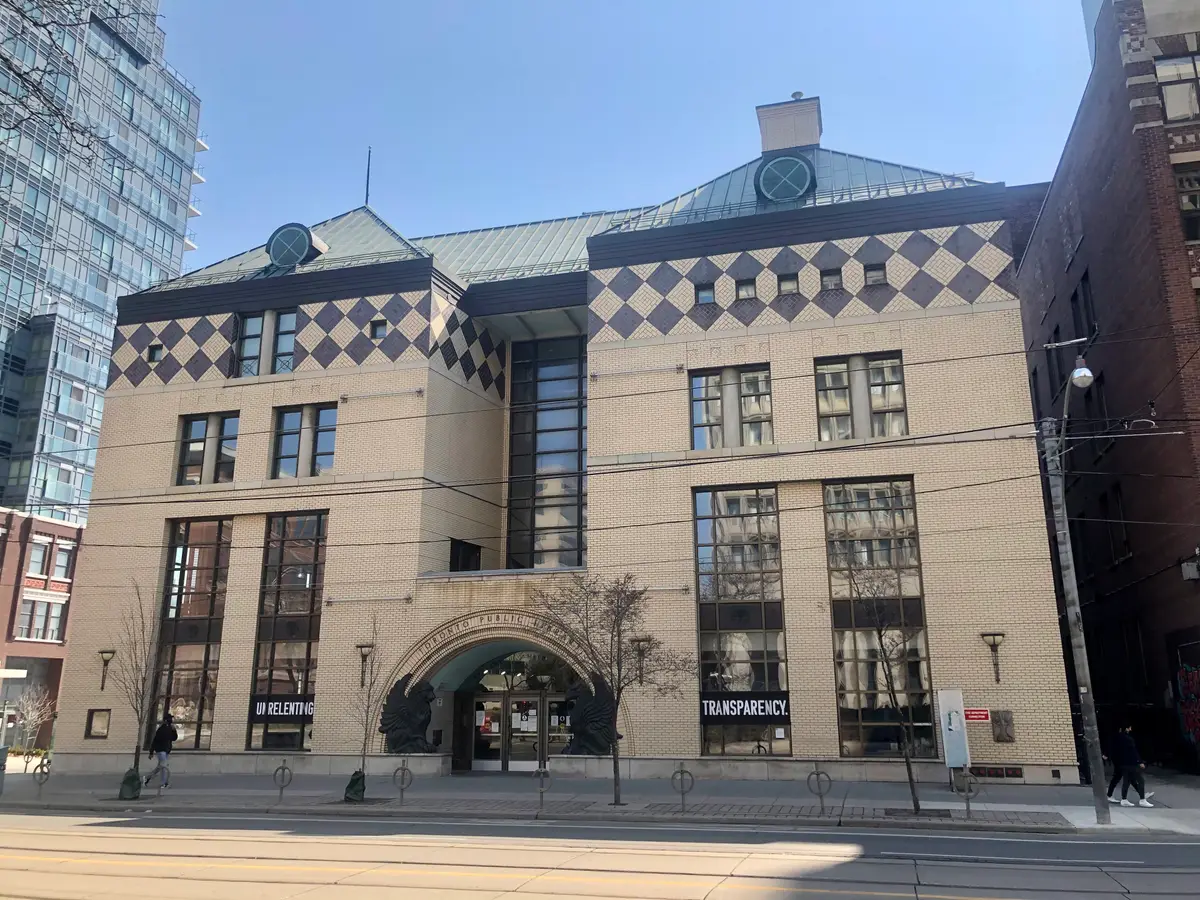 The cream stone front of the Lillian H. Smith branch of Toronto Public Library, with a diamond-patterned top floor and a glass-and-brick entrance