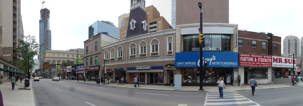A wide panorama of Yonge Street north of College on a clear day, with low storefronts and a crosswalk in the foreground