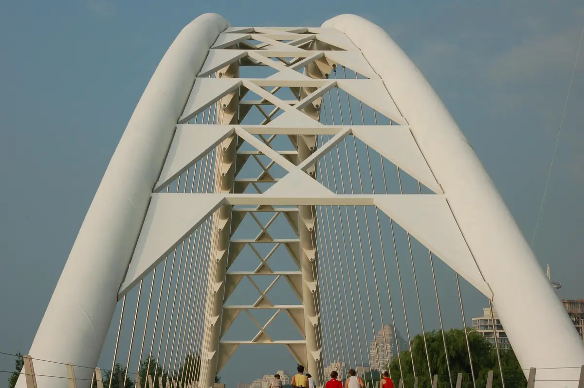 The white steel arches of the Humber Bay pedestrian bridge with walkers and cyclists ahead