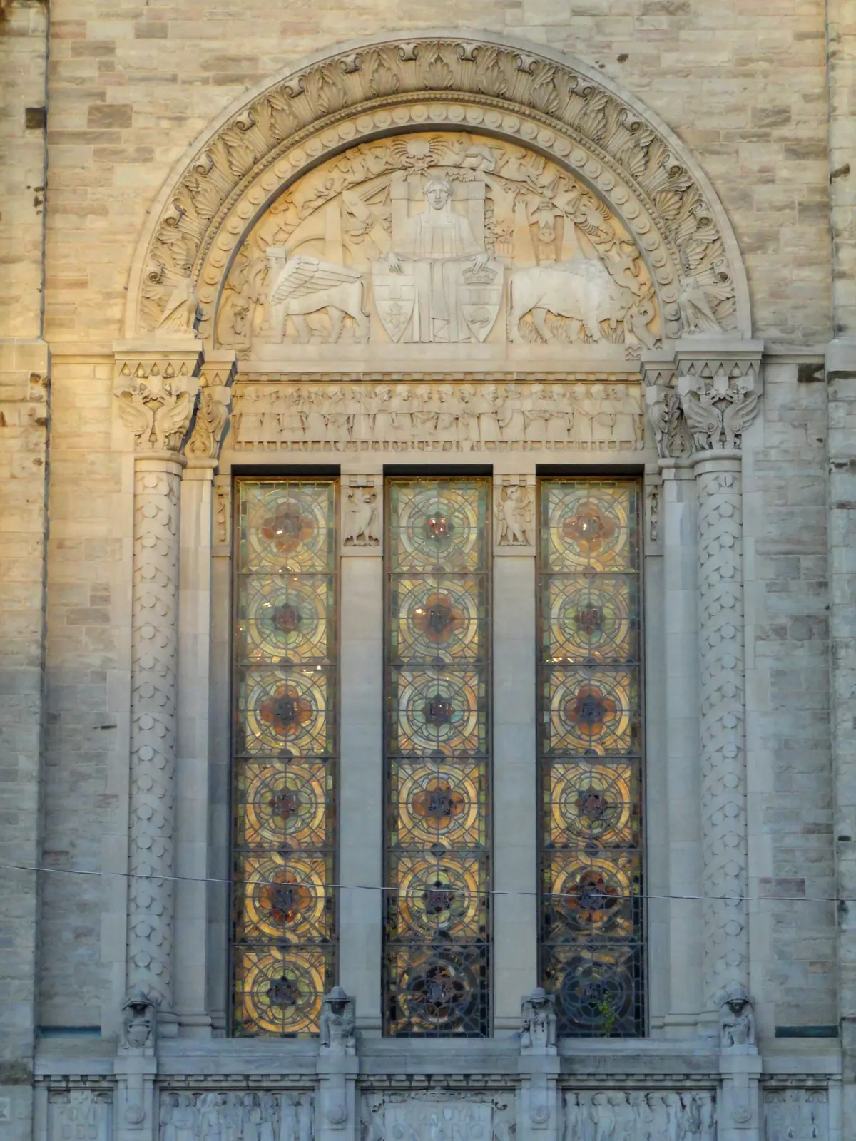 Tall stained-glass windows set in a stone facade beneath a carved arch.
