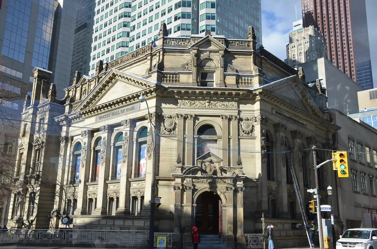Stone facade of the historic Hockey Hall of Fame building, with its name on the facade and glass towers behind.