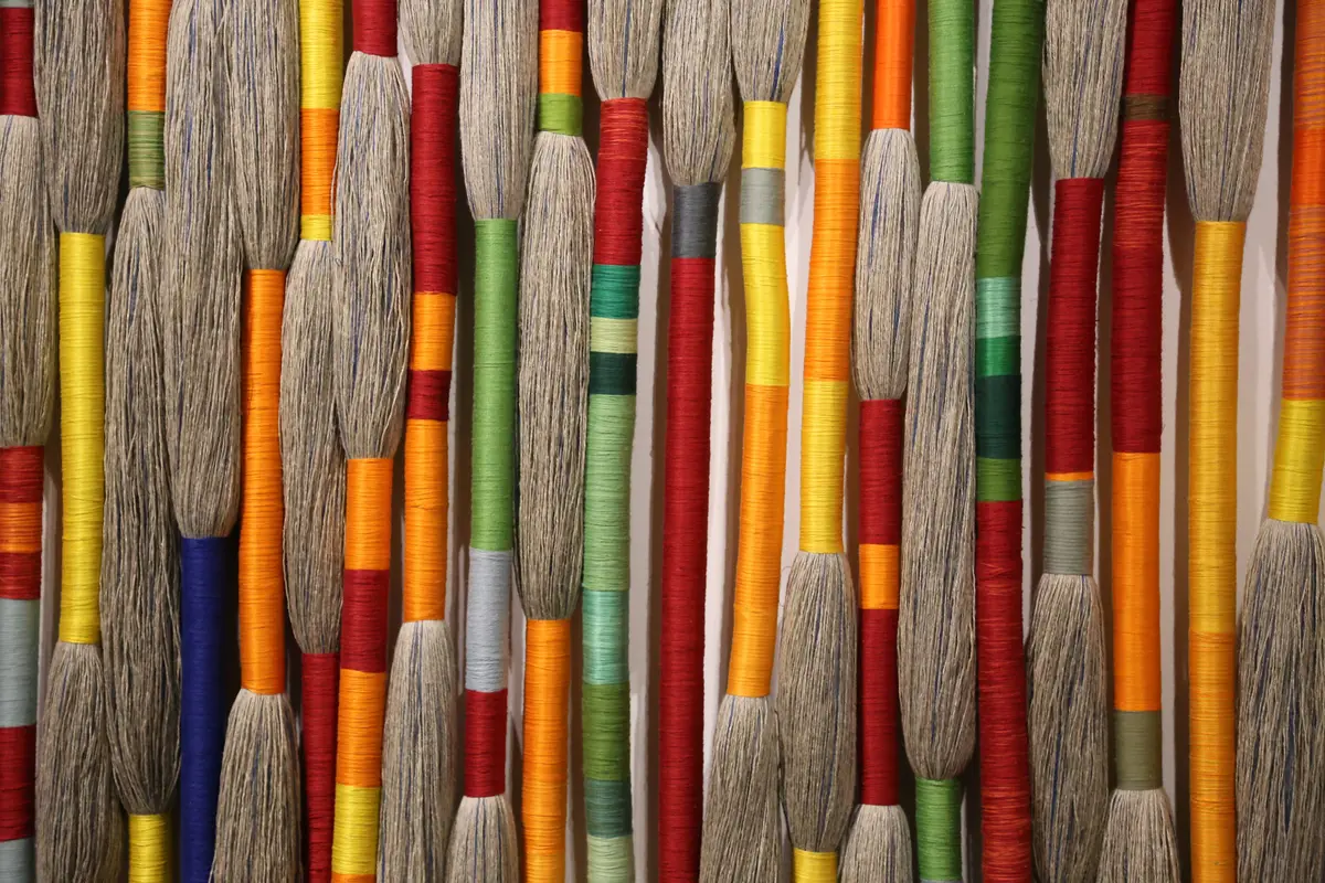 Bundles of coloured wrapped threads hang side by side on a gallery wall.