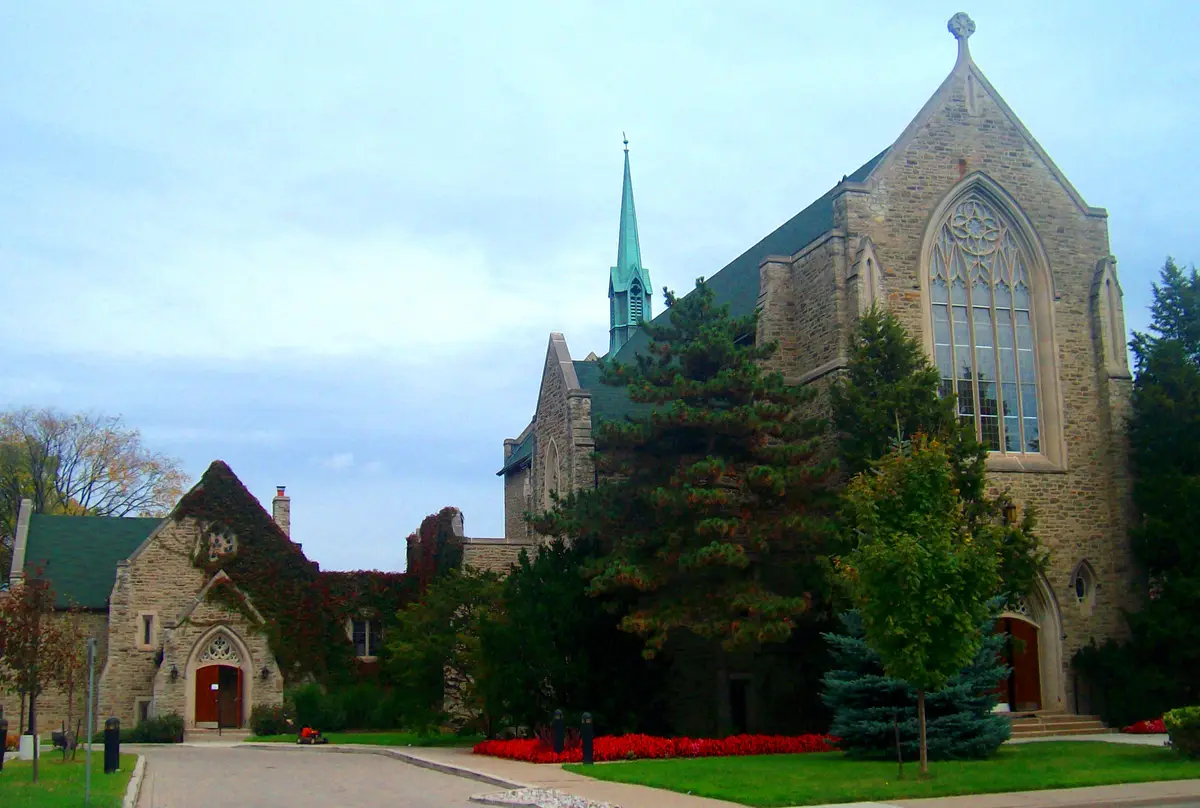 Islington United Church, a stone church with a green copper spire and a tall Gothic window, with red flowers along its lawn