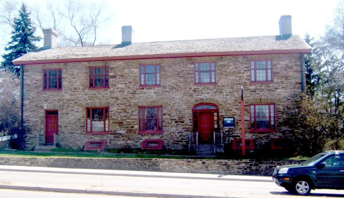 The two-storey fieldstone front of Montgomery's Inn with red doors and window frames, seen from Dundas Street West