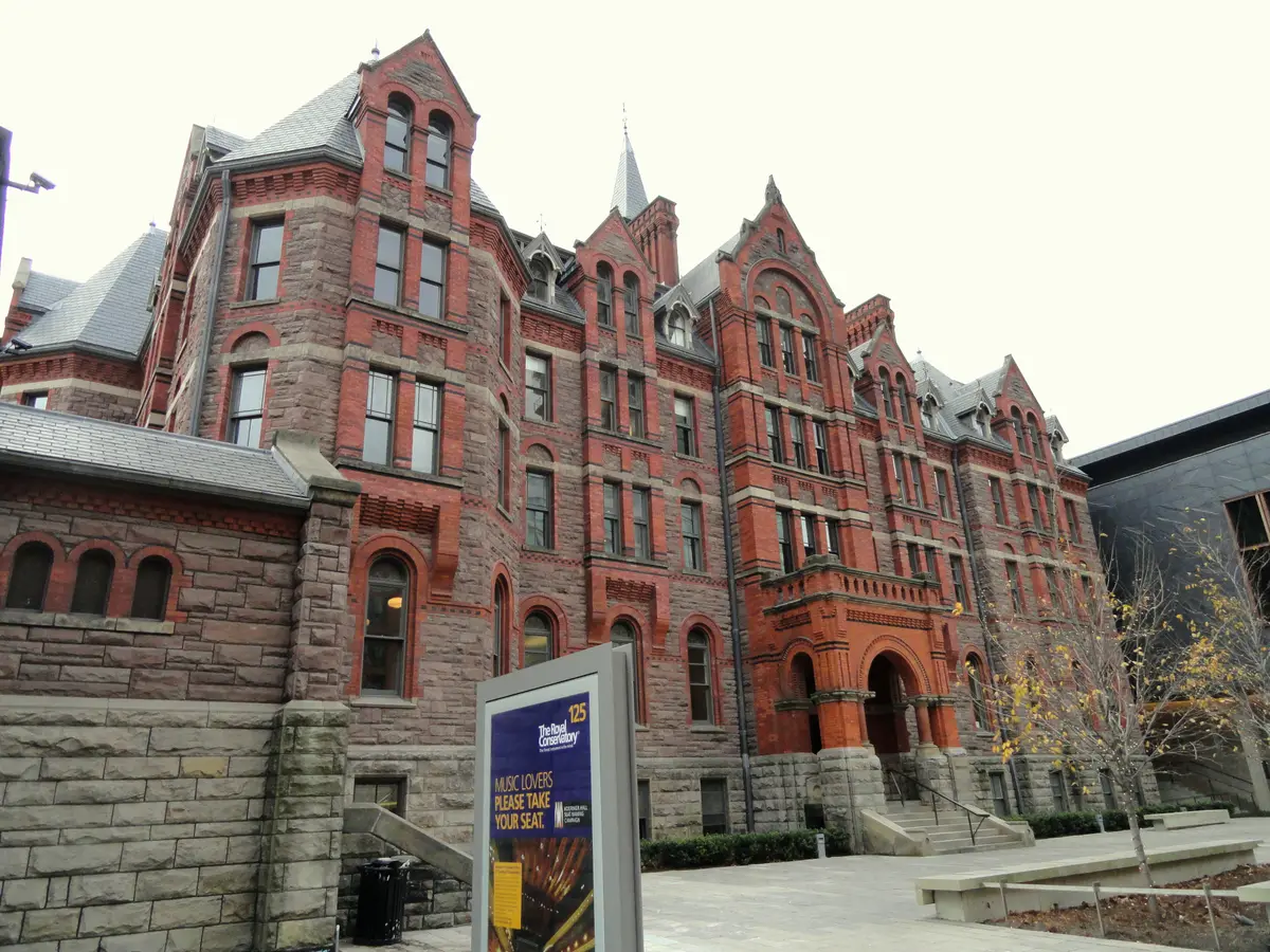 Red-brick and stone facade of the Royal Conservatory of Music, with arched doorways and steep gables under an overcast sky