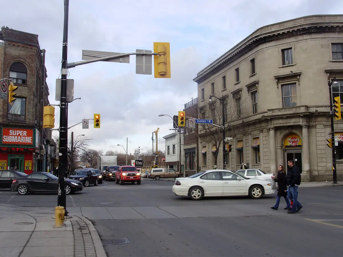 A grey-sky intersection with traffic, a cream stone corner building with a Dundas W street sign, and red-brick shops beyond