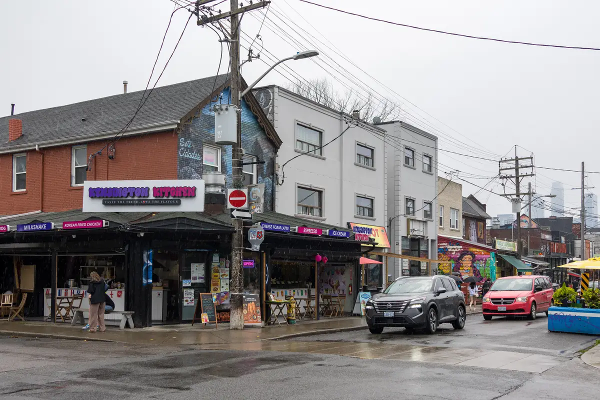 The corner of Augusta Avenue and Nassau Street on a rainy day, with food stalls, a mural and cars passing