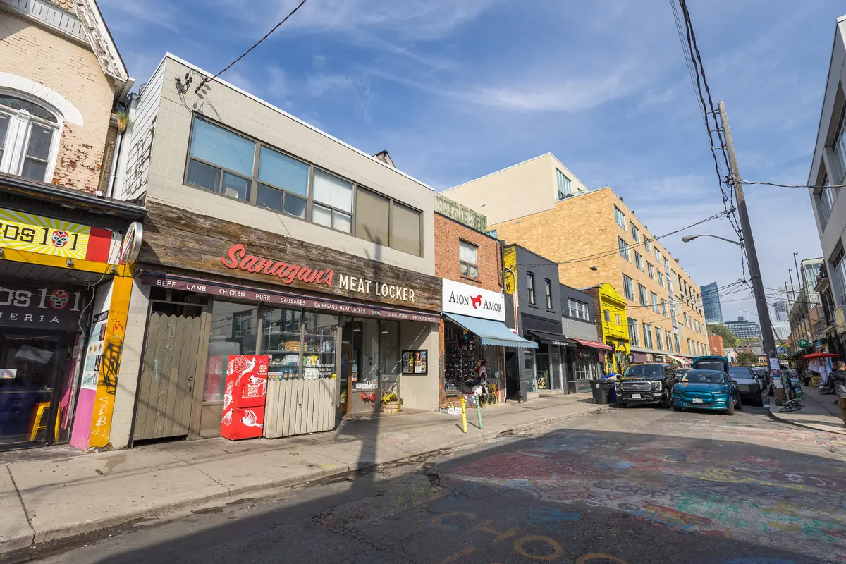 Baldwin Street in Kensington Market, with a row of colourful shopfronts under a blue sky and a street painted with chalk drawings