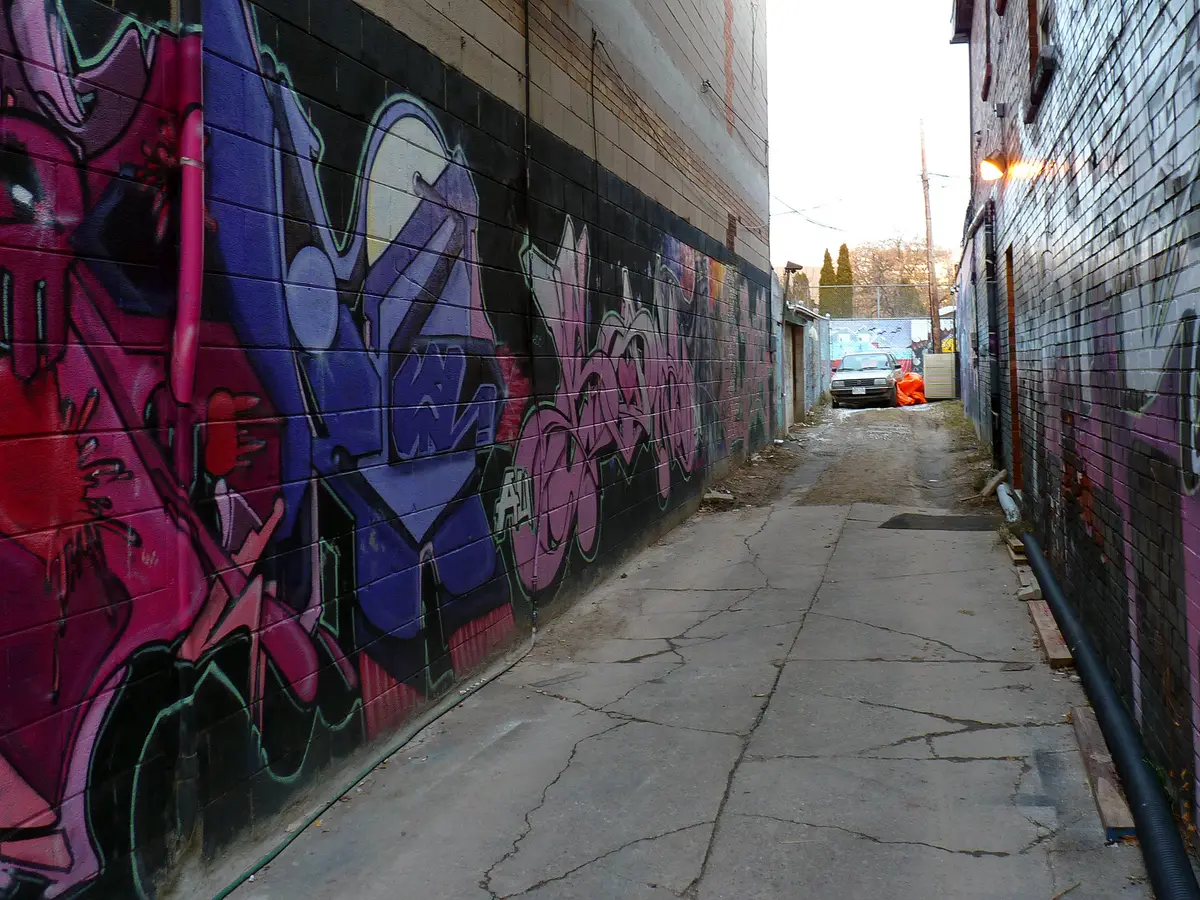 A narrow back alley in Kensington Market with painted walls and a parked car at the end