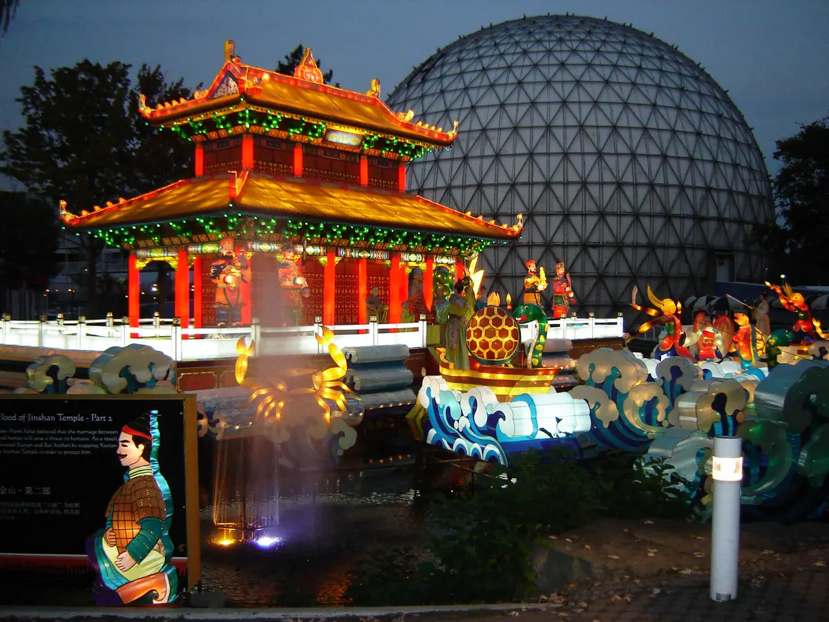 A glowing lantern display of a red pagoda and painted figures at night beside a large dome
