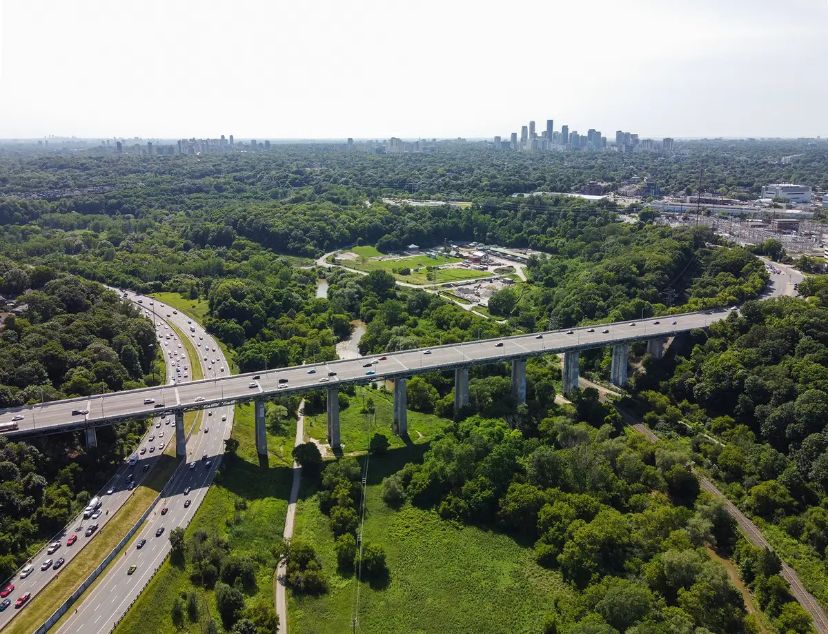 Aerial view of the Leaside Bridge arcing across the wooded Don Valley with the downtown skyline on the horizon.