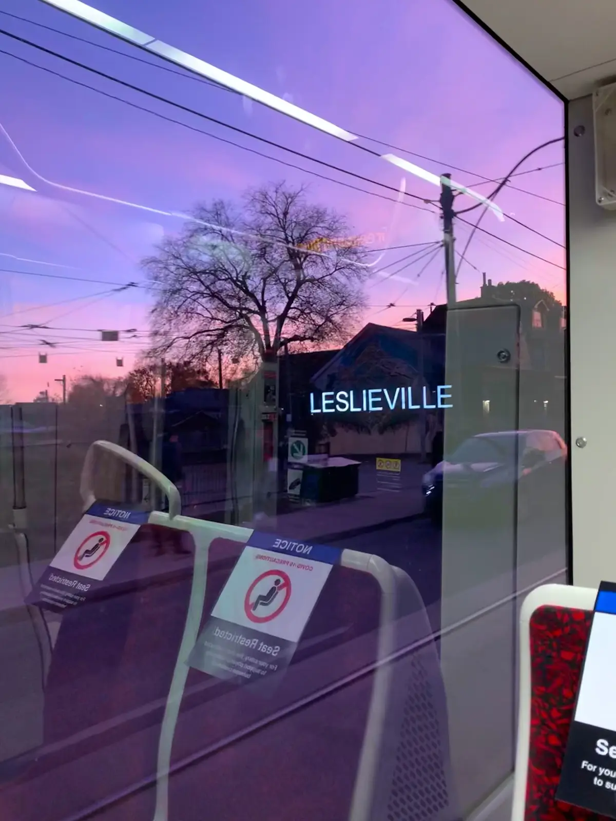 A purple evening sky and a Leslieville sign seen through a streetcar window