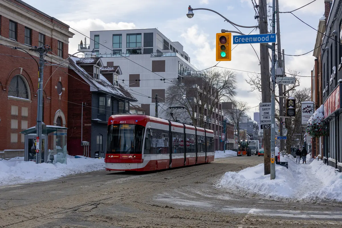A red 501 Queen streetcar heading east along snowy Queen Street at Greenwood Avenue in Leslieville