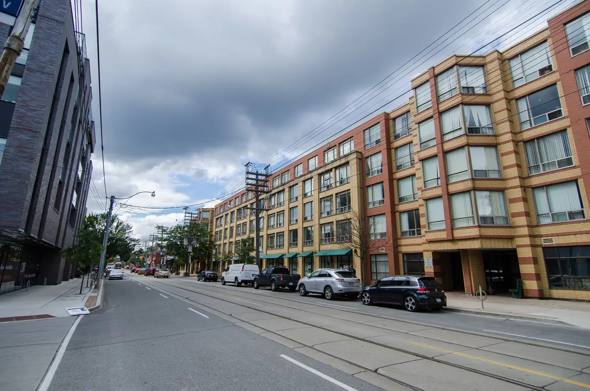 Queen Street East and its streetcar tracks near Winnifred Avenue, with trees and apartment buildings along the north side