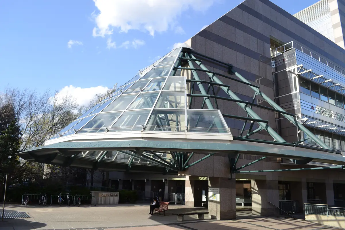 Glass pyramid on the front of North York Central Library under a blue sky, with a person seated on a bench in the plaza