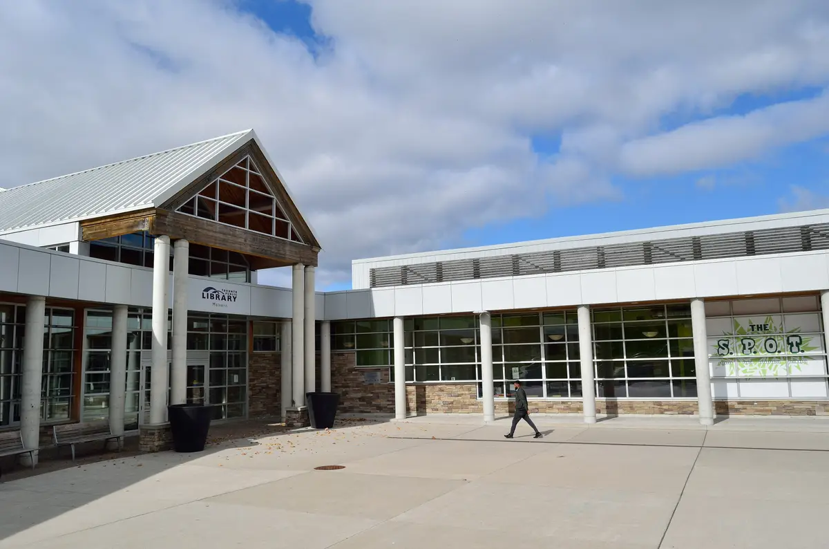Front of the Malvern branch, with a timber-framed entrance under a metal gable roof and a person walking across the paved plaza under a partly cloudy sky.