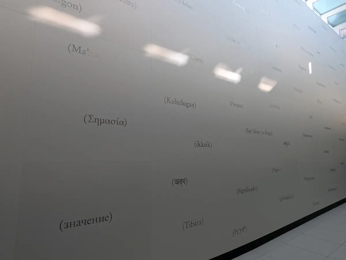 A pale wall covered in the word meaning written in many languages and scripts at Kennedy Station.