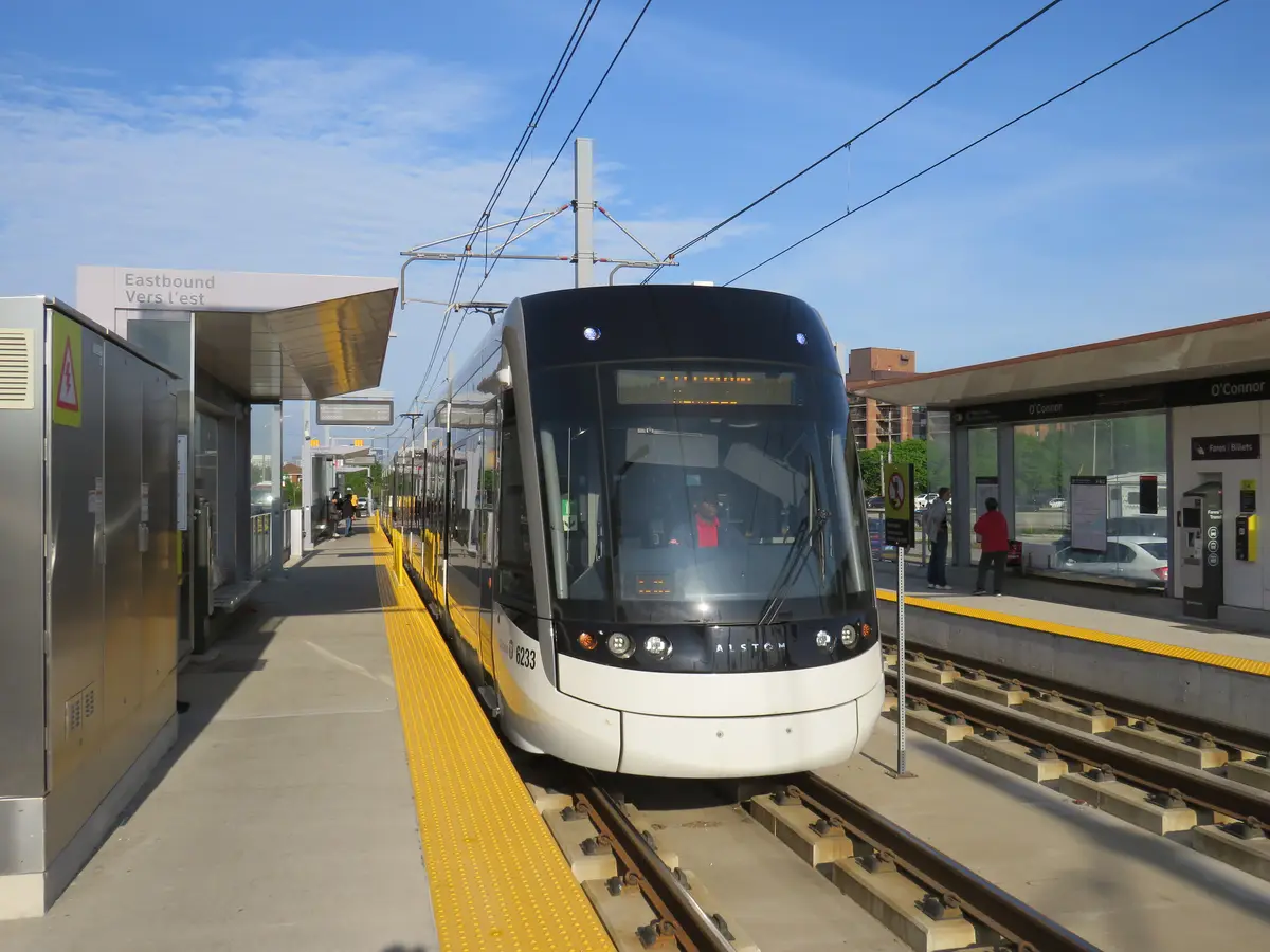 A Line 5 Eglinton light rail vehicle pulling into a street-level stop on a clear day.