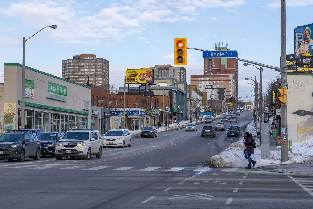 Eglinton Avenue at Keele Street in winter, with traffic, shopfronts and snow piled at the curb