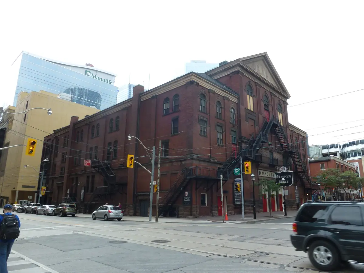 Red-brick Massey Hall with a gabled front and iron fire escapes on a city street corner.