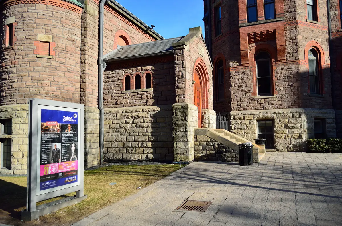 Stone and red-brick building with arched doorways, with a TELUS Centre concert poster on the sidewalk.