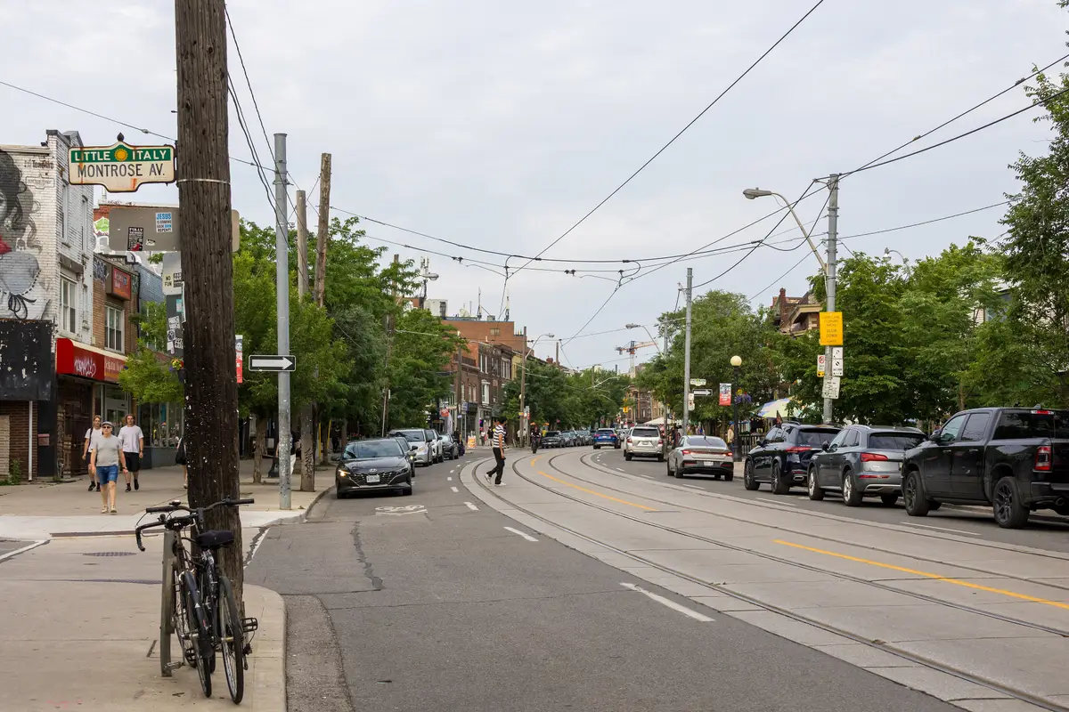 College Street at Montrose Avenue, with a Little Italy street sign, streetcar tracks and parked cars under green trees