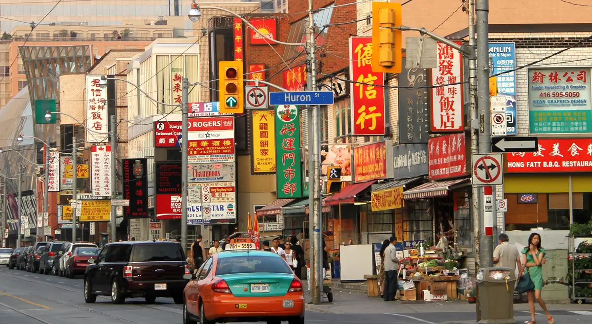 Dundas Street at Huron Street in Chinatown, with Chinese-language shop signs, a Huron Street sign and pedestrians on the sidewalk