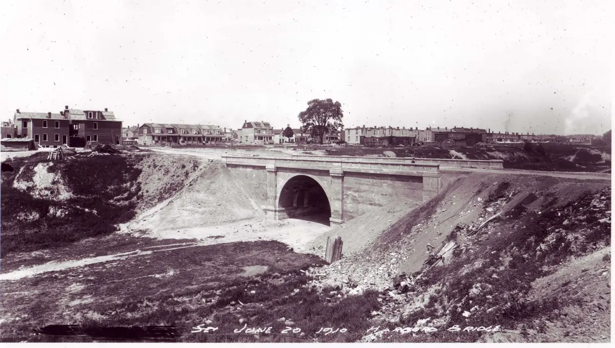 Sepia photograph of a stone arch bridge spanning a dug-out ravine, with rows of houses on the far side