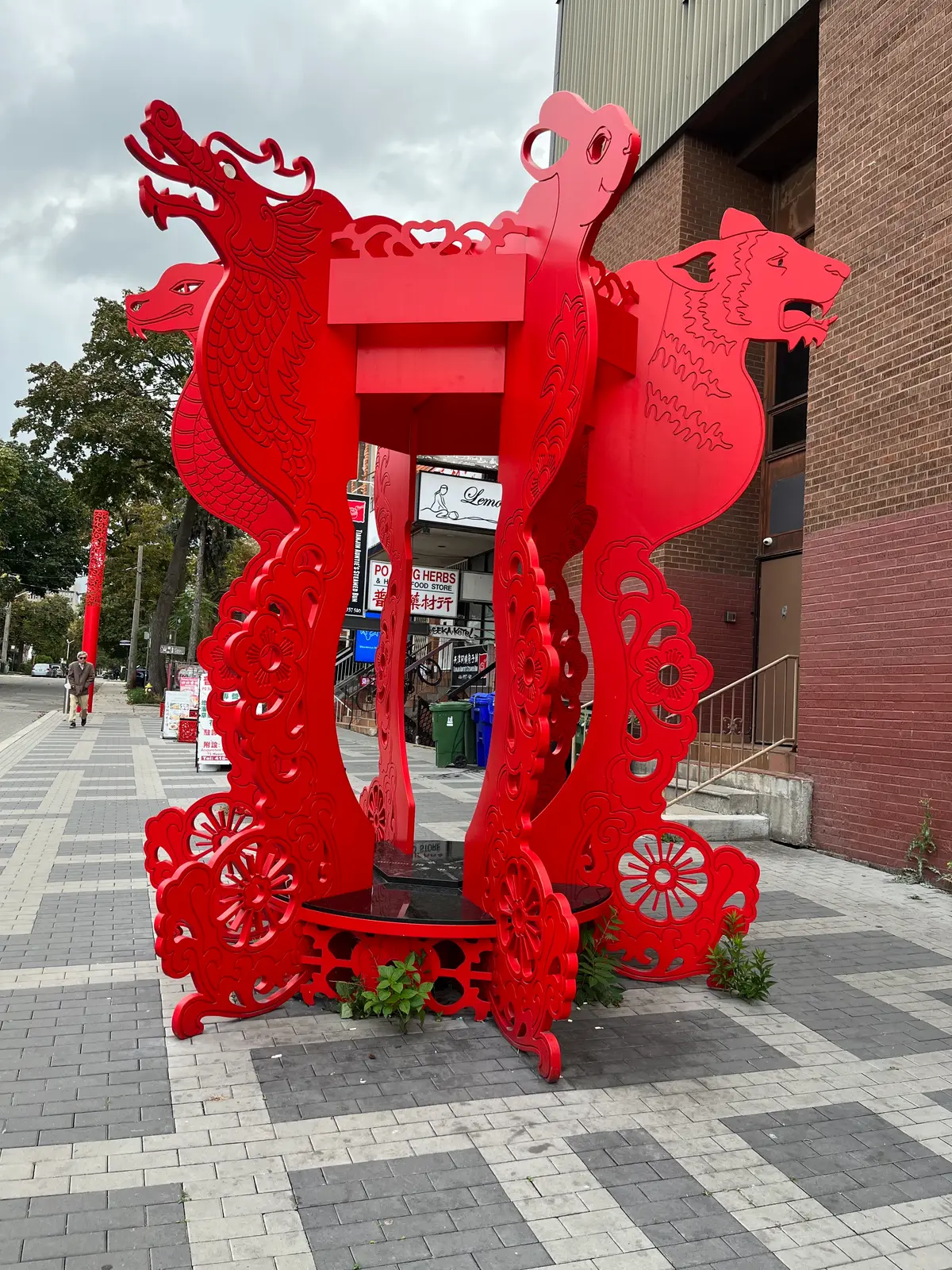 A tall red openwork sculpture with dragon and animal shapes on a paved plaza.