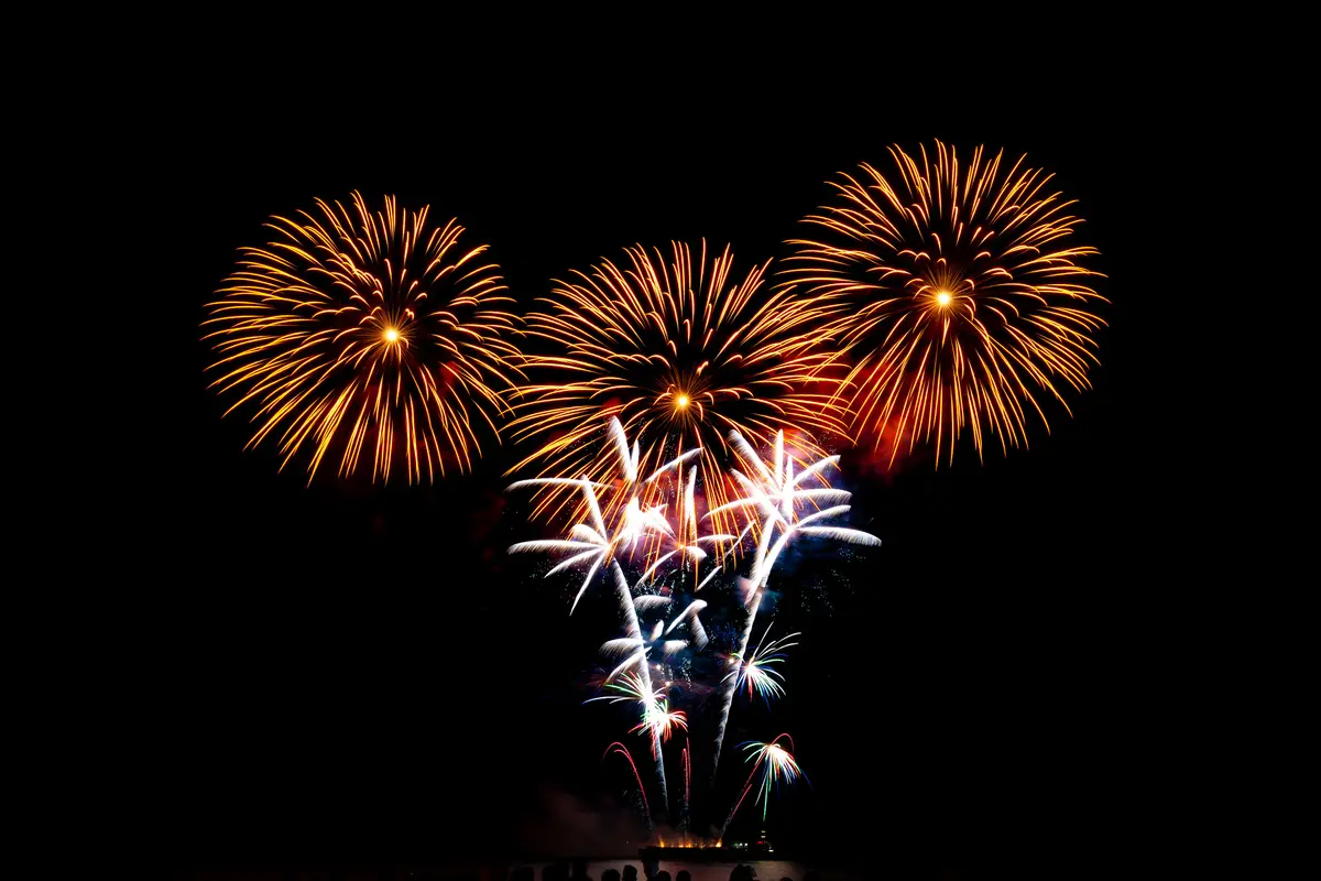 Fireworks bursting in orange and white against a black night sky over the Toronto waterfront