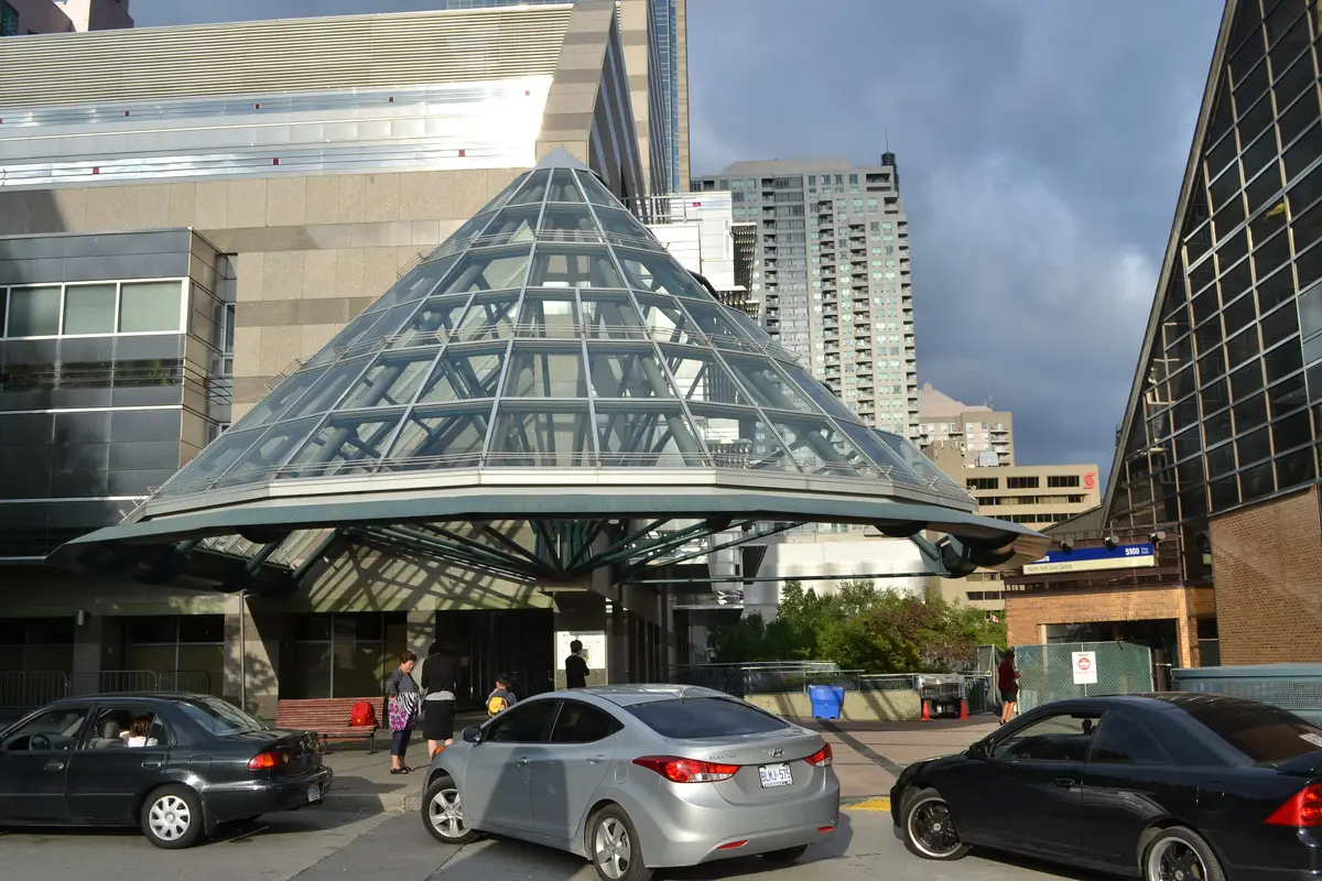 The glass pyramid entrance of the North York Central Library, with cars at the curb and office towers behind
