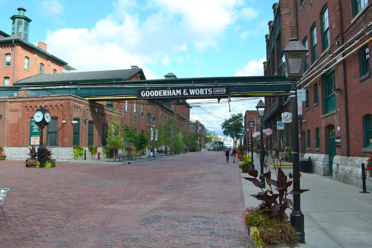A brick street lined with red-brick buildings, street lamps and a Gooderham and Worts sign overhead