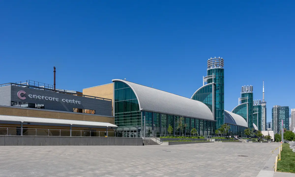 The glass and steel front of the Enercare Centre at Exhibition Place with a tower in the distance