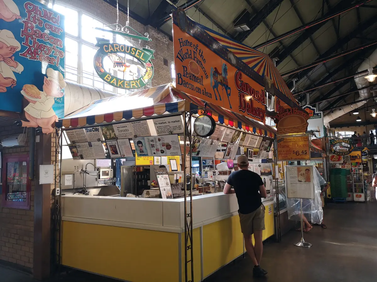 The Carousel Bakery stall at St. Lawrence Market, with a carousel sign above a yellow counter and a customer ordering