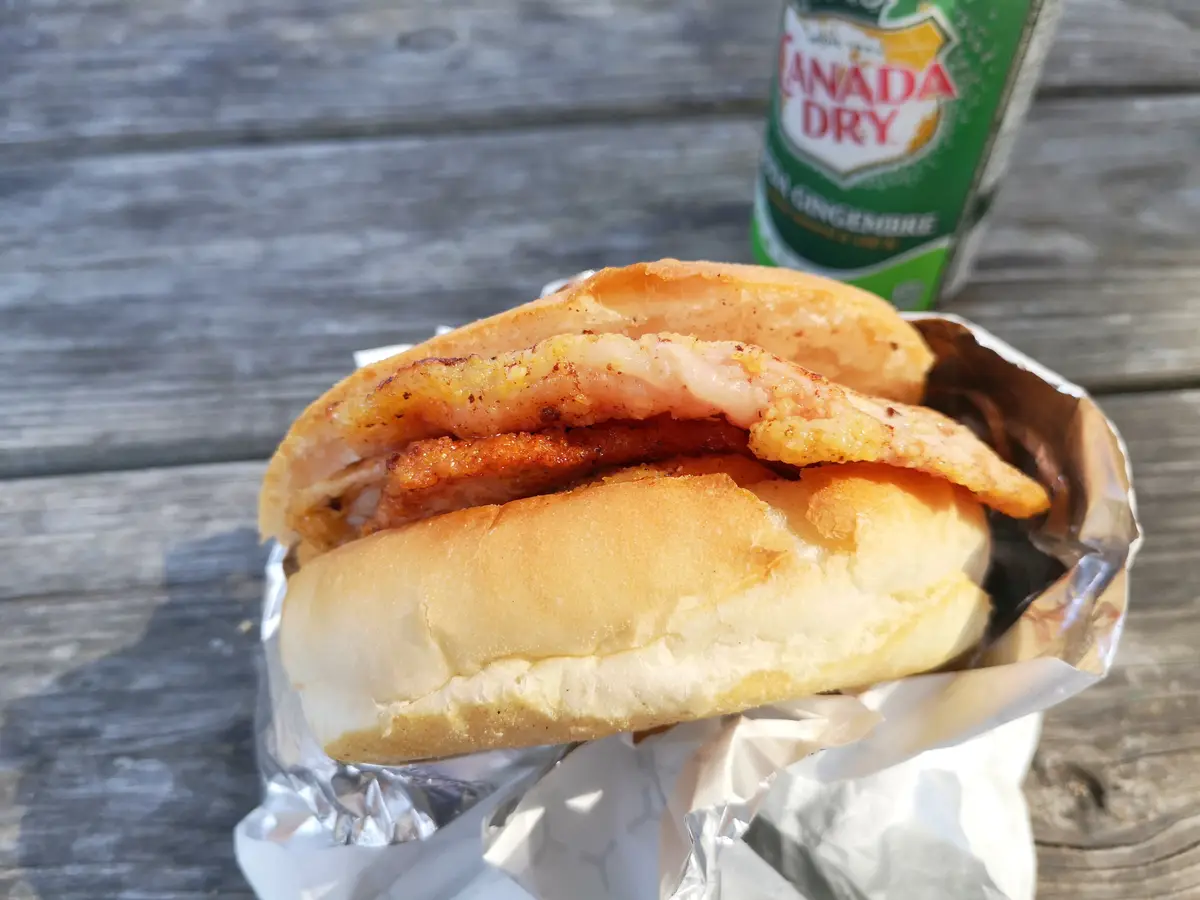 A peameal bacon sandwich from Carousel Bakery, wrapped in foil on a weathered wooden table beside a can of ginger ale