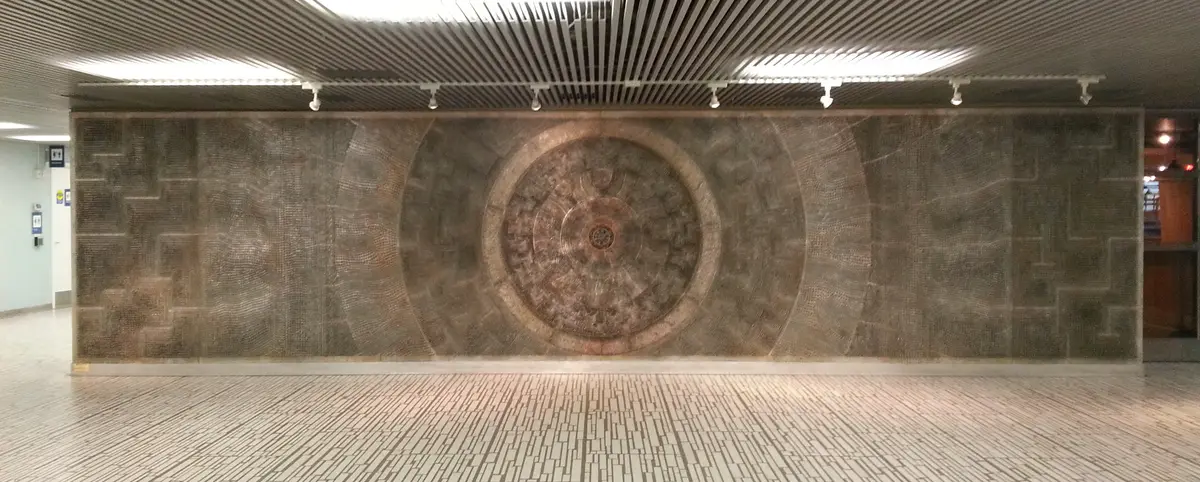 David Partridge's Metropolis, a long wall of textured metal panels with a circular design at the centre, in an indoor passage
