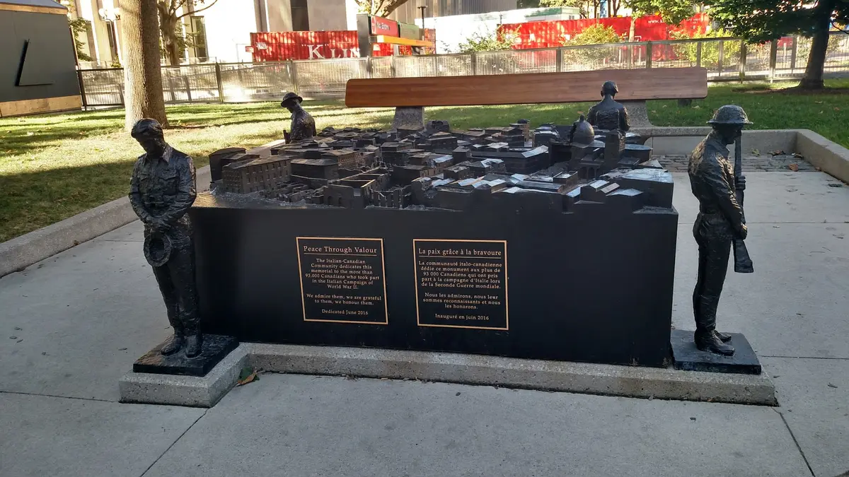 Peace Through Valour: a dark memorial with a model town on top, four soldier figures around its edges and a plaque on the front