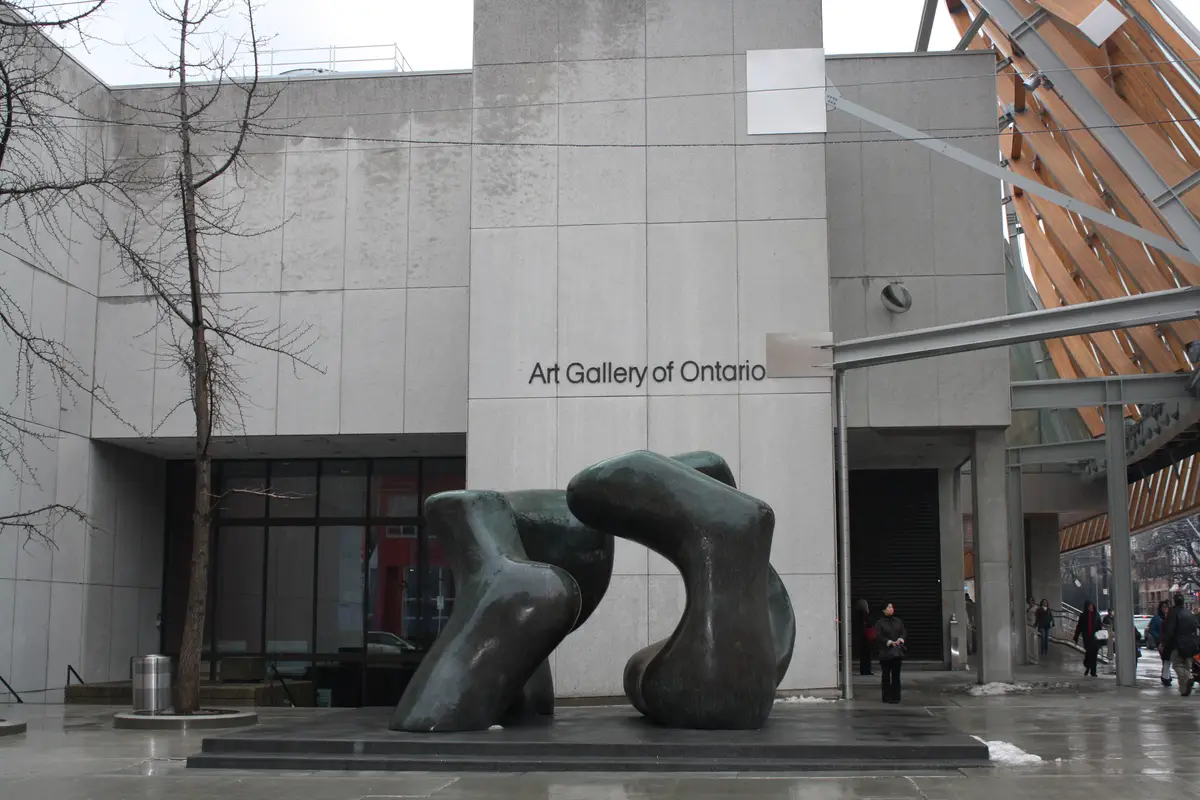 Wet pavement in front of the Art Gallery of Ontario, where a large bronze sculpture stands by the entrance