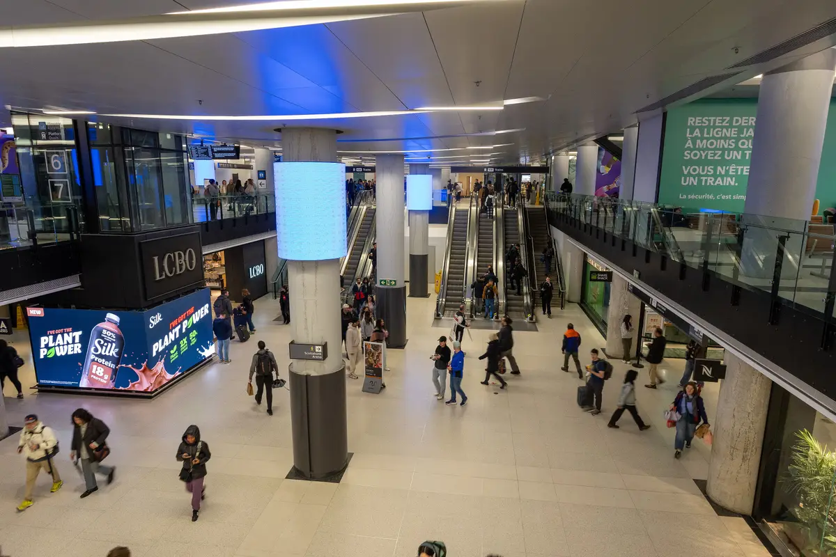 Commuters crossing a bright concourse with escalators and shops